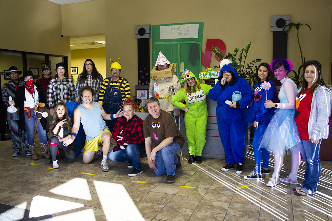 a group of people posing for a picture in Halloween costumes in front of a Sesame Street sign